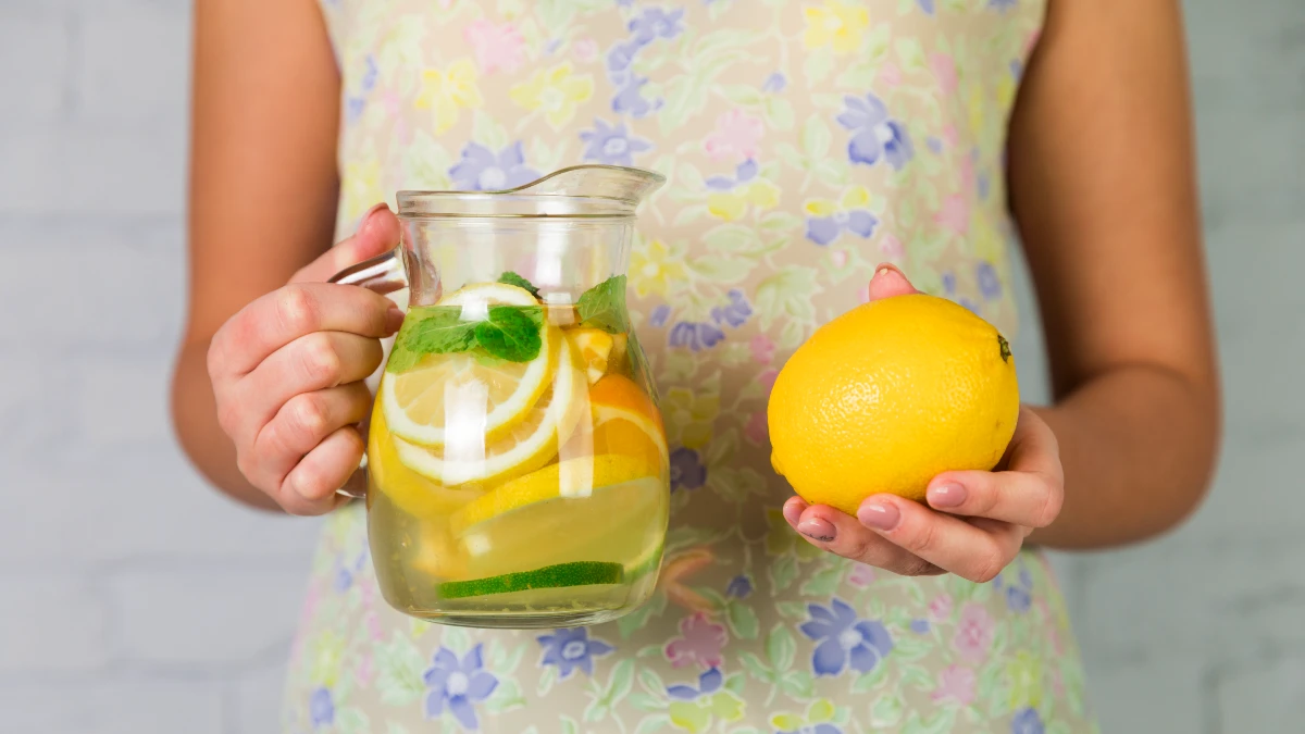Mature hands squeeze fresh lemon juice into glass of water for improved nutrient absorption